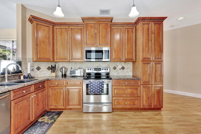 kitchen featuring stainless steel appliances, sink, pendant lighting, and stone counters