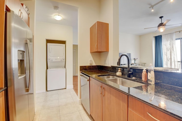 kitchen with stacked washer and dryer, sink, light tile patterned floors, appliances with stainless steel finishes, and dark stone counters