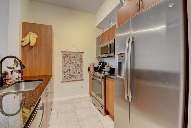 kitchen featuring dark stone countertops, stainless steel appliances, sink, and light tile patterned floors