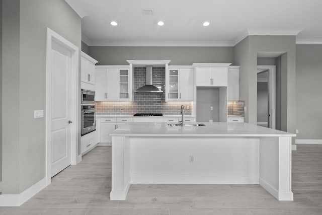 kitchen with wall chimney exhaust hood, sink, white cabinetry, appliances with stainless steel finishes, and a kitchen island with sink