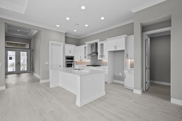 kitchen with appliances with stainless steel finishes, sink, white cabinets, wall chimney range hood, and a center island with sink