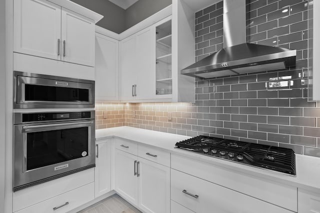 kitchen with appliances with stainless steel finishes, white cabinets, backsplash, and wall chimney exhaust hood