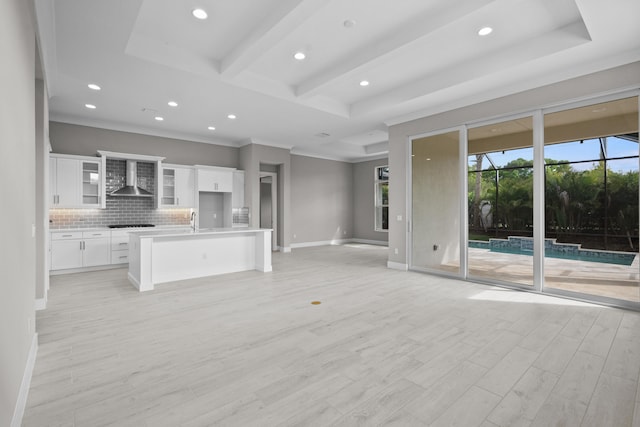 unfurnished living room featuring sink, light wood-type flooring, ornamental molding, a tray ceiling, and beamed ceiling