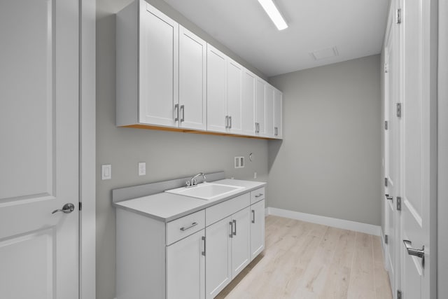 laundry room featuring sink, hookup for a washing machine, cabinets, and light wood-type flooring