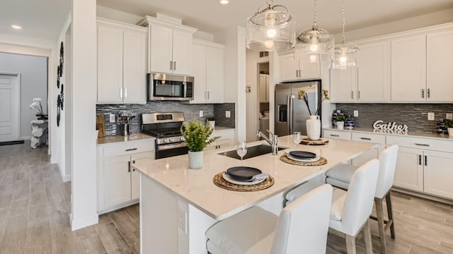 kitchen with sink, decorative light fixtures, a center island with sink, stainless steel appliances, and white cabinets