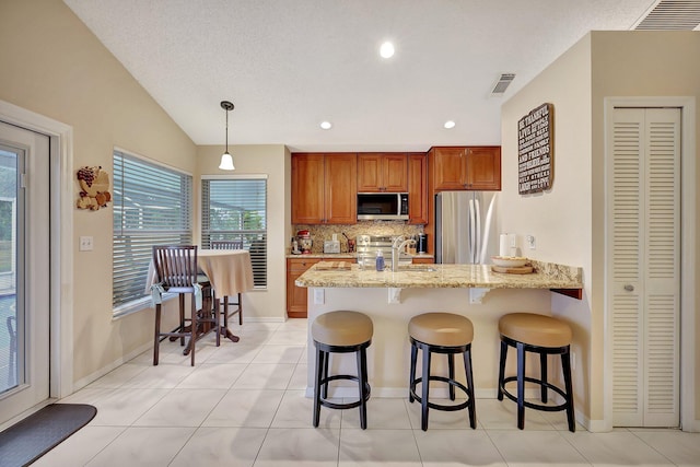 kitchen with pendant lighting, lofted ceiling, stainless steel appliances, light stone countertops, and kitchen peninsula