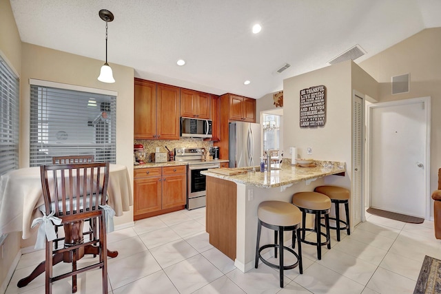 kitchen featuring tasteful backsplash, hanging light fixtures, appliances with stainless steel finishes, kitchen peninsula, and light stone countertops