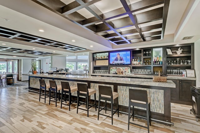 bar with beam ceiling, light stone countertops, coffered ceiling, and light hardwood / wood-style floors