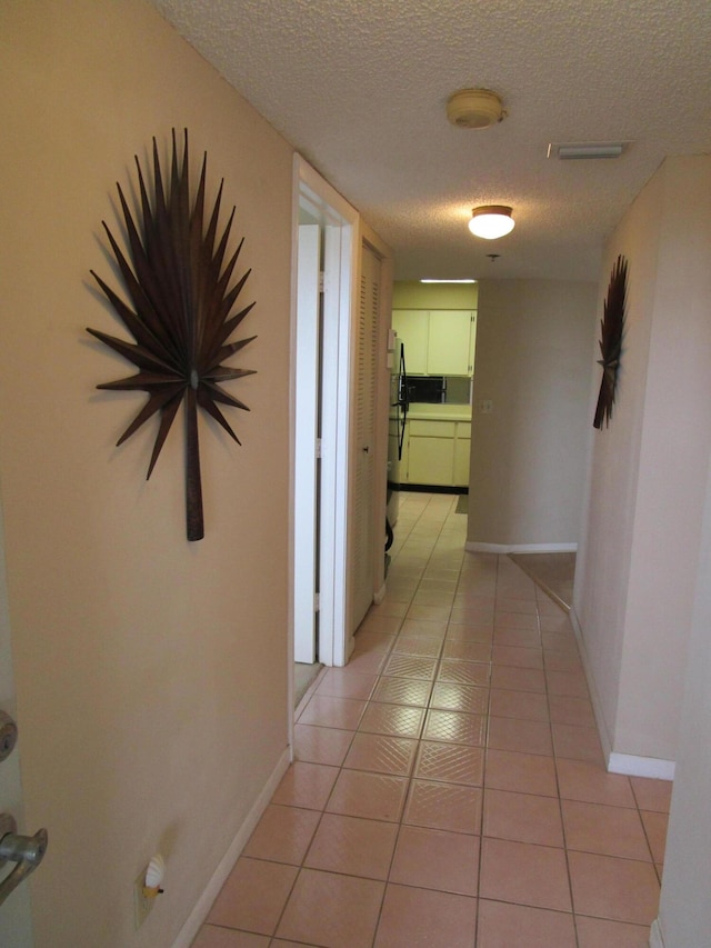 corridor featuring a textured ceiling and light tile patterned floors