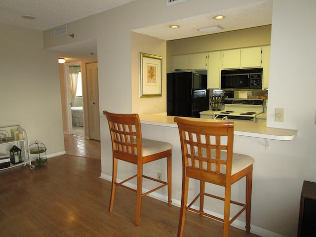 kitchen featuring a breakfast bar, black appliances, white cabinets, kitchen peninsula, and dark wood-type flooring