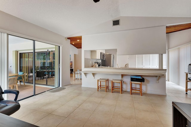 kitchen featuring visible vents, a kitchen breakfast bar, appliances with stainless steel finishes, light tile patterned flooring, and lofted ceiling