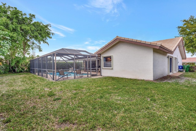 rear view of house with glass enclosure, a lawn, an outdoor pool, and stucco siding