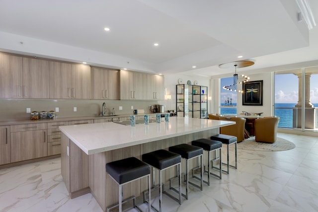 kitchen with a large island, sink, a water view, light stone counters, and light brown cabinets