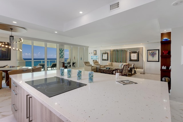 kitchen featuring pendant lighting, an inviting chandelier, a water view, light stone counters, and black electric cooktop