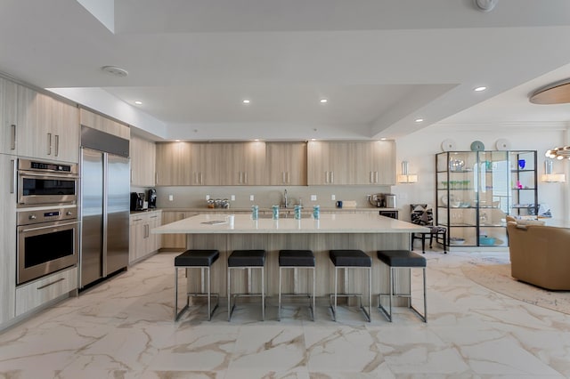 kitchen with light brown cabinets, appliances with stainless steel finishes, a center island with sink, and a kitchen breakfast bar