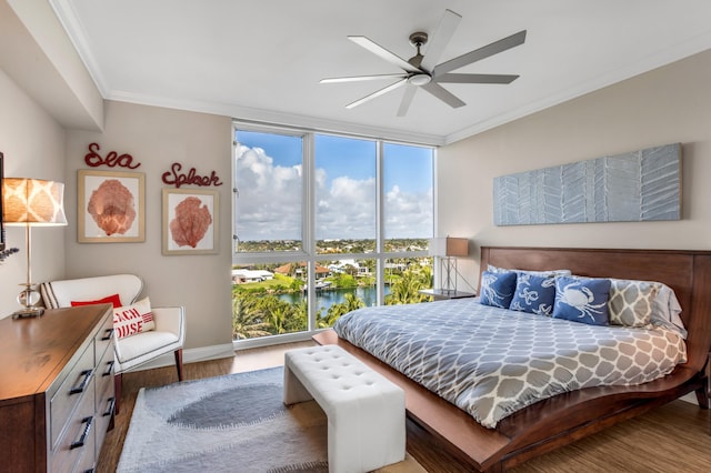 bedroom with crown molding, a wall of windows, ceiling fan, a water view, and wood-type flooring