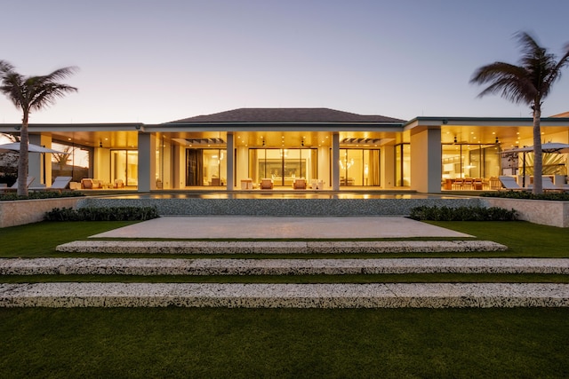 back house at dusk featuring a patio and a lawn