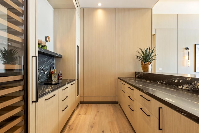 kitchen with dark stone countertops, light hardwood / wood-style flooring, and light brown cabinetry