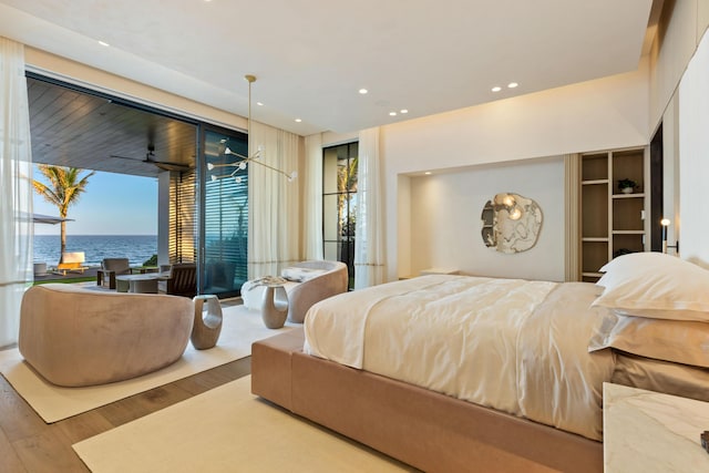 bedroom with multiple windows, access to outside, a water view, and wood-type flooring