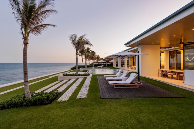 yard at dusk with a patio, a water view, and ceiling fan