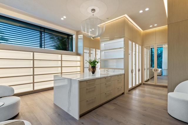 walk in closet with decorative light fixtures, light wood-type flooring, and light stone countertops