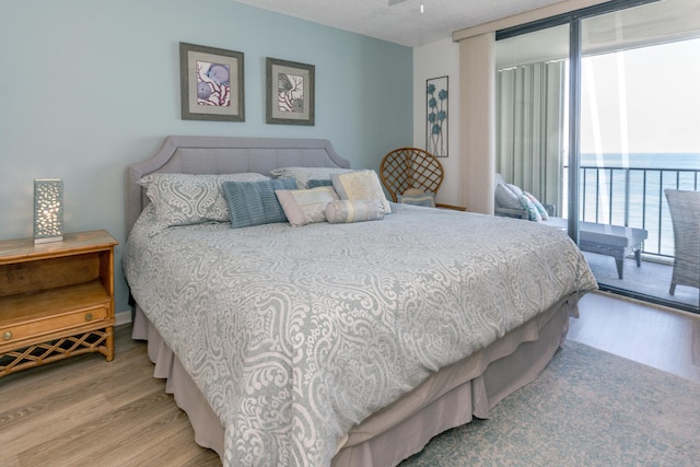 bedroom with multiple windows, a water view, access to exterior, and light wood-type flooring