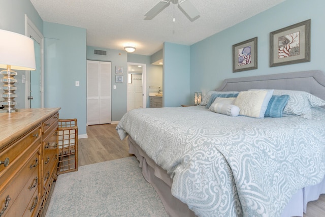 bedroom featuring ensuite bathroom, ceiling fan, a textured ceiling, light wood-type flooring, and a closet