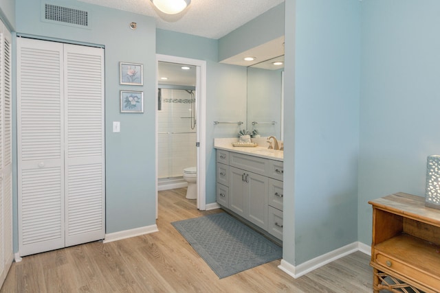 bathroom with hardwood / wood-style flooring, vanity, toilet, and walk in shower