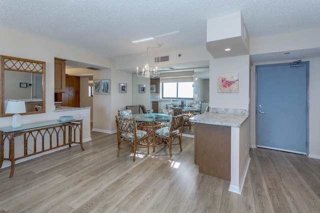 kitchen with pendant lighting, a chandelier, light hardwood / wood-style floors, kitchen peninsula, and a textured ceiling