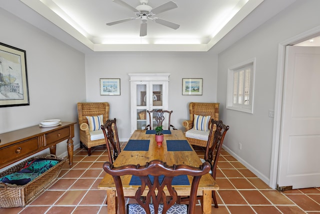 dining space with ceiling fan, a tray ceiling, and tile patterned flooring