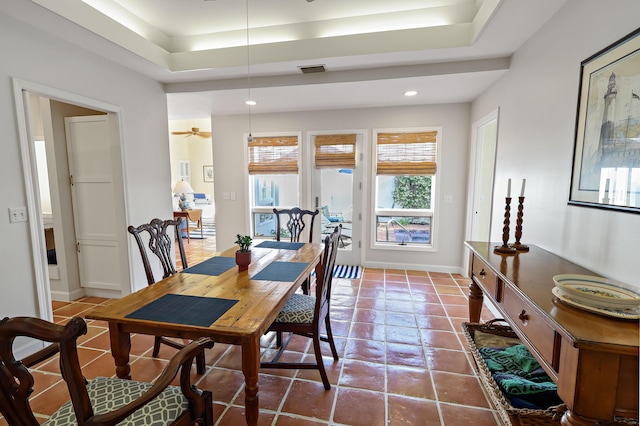 tiled dining room with ceiling fan and a tray ceiling