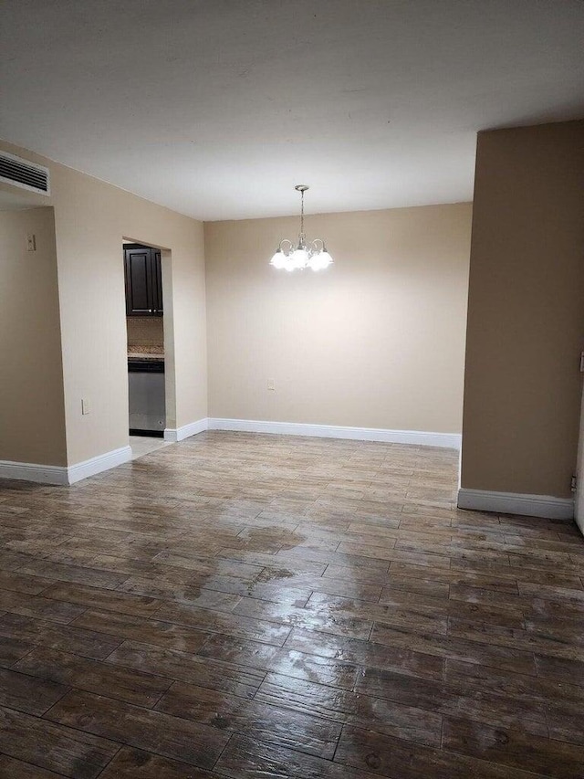 spare room with dark hardwood / wood-style floors and a notable chandelier