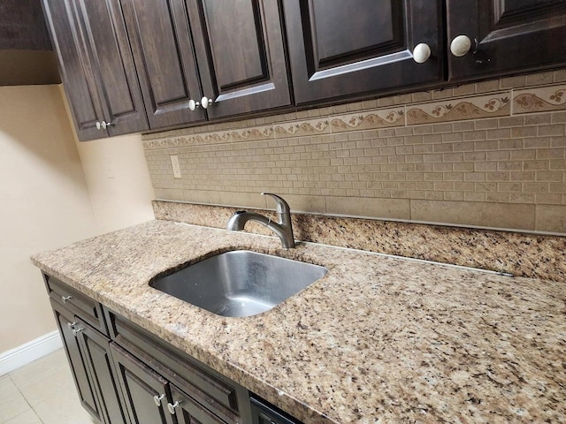 kitchen with light tile patterned flooring, sink, backsplash, light stone countertops, and dark brown cabinets