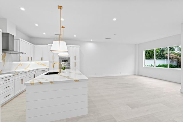 kitchen with a spacious island, wall chimney exhaust hood, sink, white cabinetry, and pendant lighting