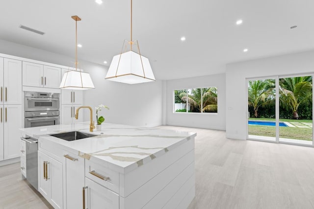 kitchen featuring sink, white cabinetry, a kitchen island with sink, hanging light fixtures, and light stone countertops