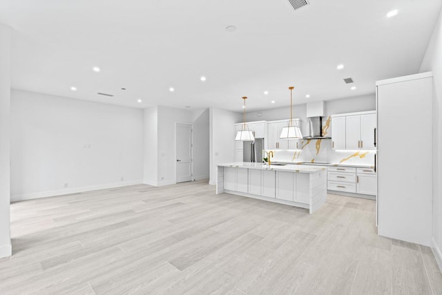 kitchen with wall chimney exhaust hood, sink, white cabinetry, decorative light fixtures, and an island with sink