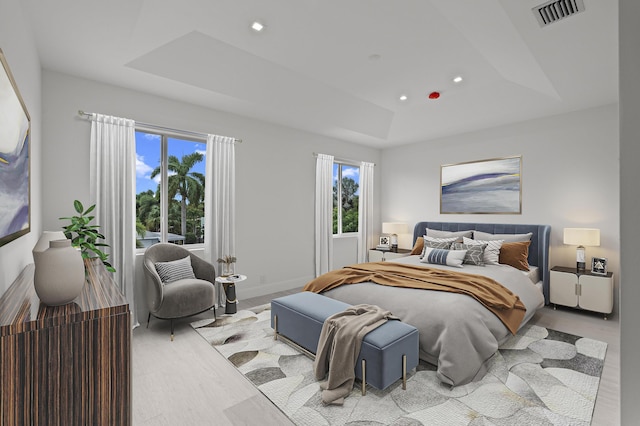 bedroom featuring multiple windows, a tray ceiling, and light hardwood / wood-style floors