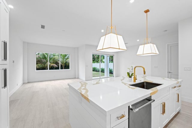 kitchen featuring pendant lighting, white cabinetry, sink, stainless steel dishwasher, and a center island with sink