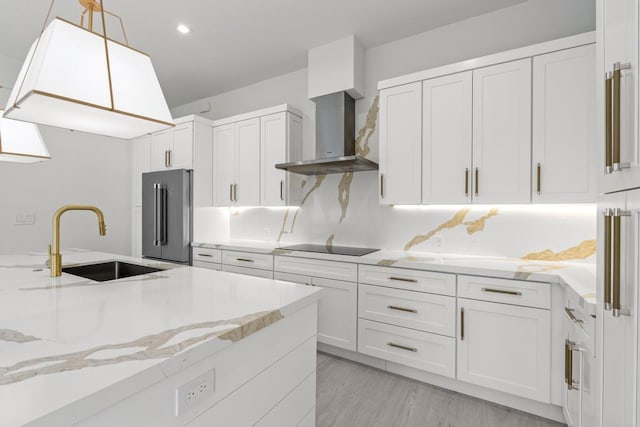 kitchen with sink, white cabinetry, high end refrigerator, decorative light fixtures, and wall chimney range hood