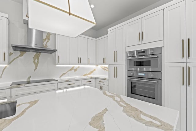 kitchen with double oven, light stone counters, black electric stovetop, white cabinets, and wall chimney exhaust hood