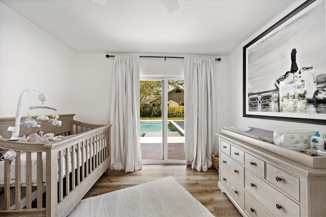 bedroom featuring a nursery area, a textured ceiling, and light hardwood / wood-style floors