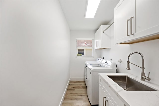 clothes washing area with sink, washing machine and dryer, cabinets, and light wood-type flooring