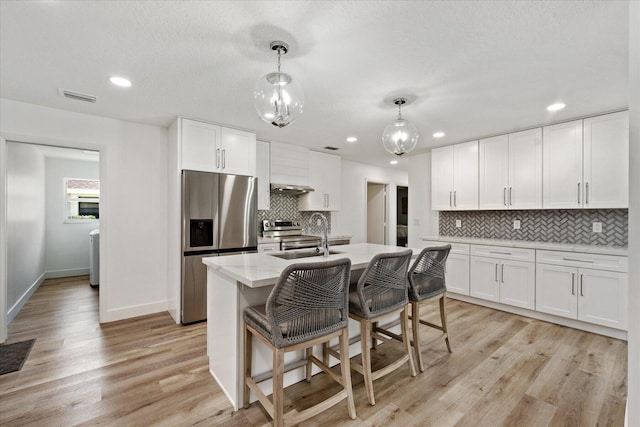 kitchen with light stone counters, pendant lighting, stainless steel appliances, a kitchen island with sink, and white cabinets