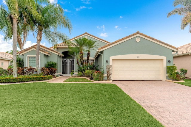 mediterranean / spanish-style home with a front yard, an attached garage, stucco siding, a tiled roof, and decorative driveway