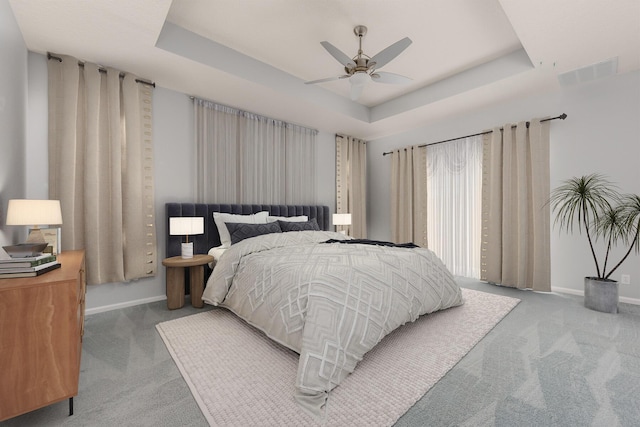 carpeted bedroom with visible vents, ceiling fan, baseboards, and a tray ceiling