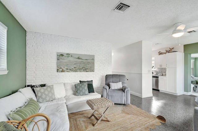 living room featuring ceiling fan, a textured ceiling, and brick wall