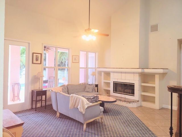 tiled living area featuring visible vents, a high ceiling, a fireplace, baseboards, and ceiling fan