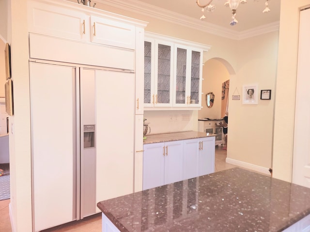 kitchen with dark stone counters, arched walkways, glass insert cabinets, white cabinetry, and crown molding