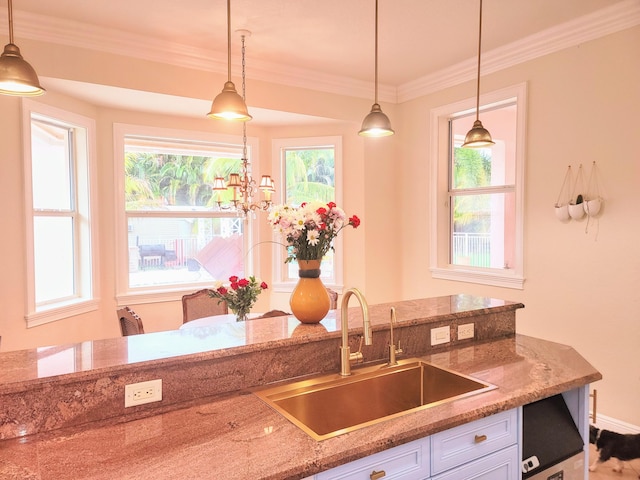 kitchen featuring ornamental molding, a sink, light stone counters, white cabinetry, and hanging light fixtures