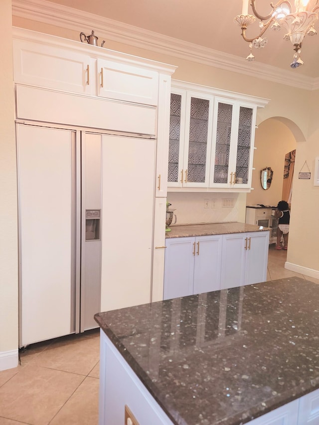 kitchen featuring dark stone counters, ornamental molding, light tile patterned flooring, arched walkways, and white cabinetry